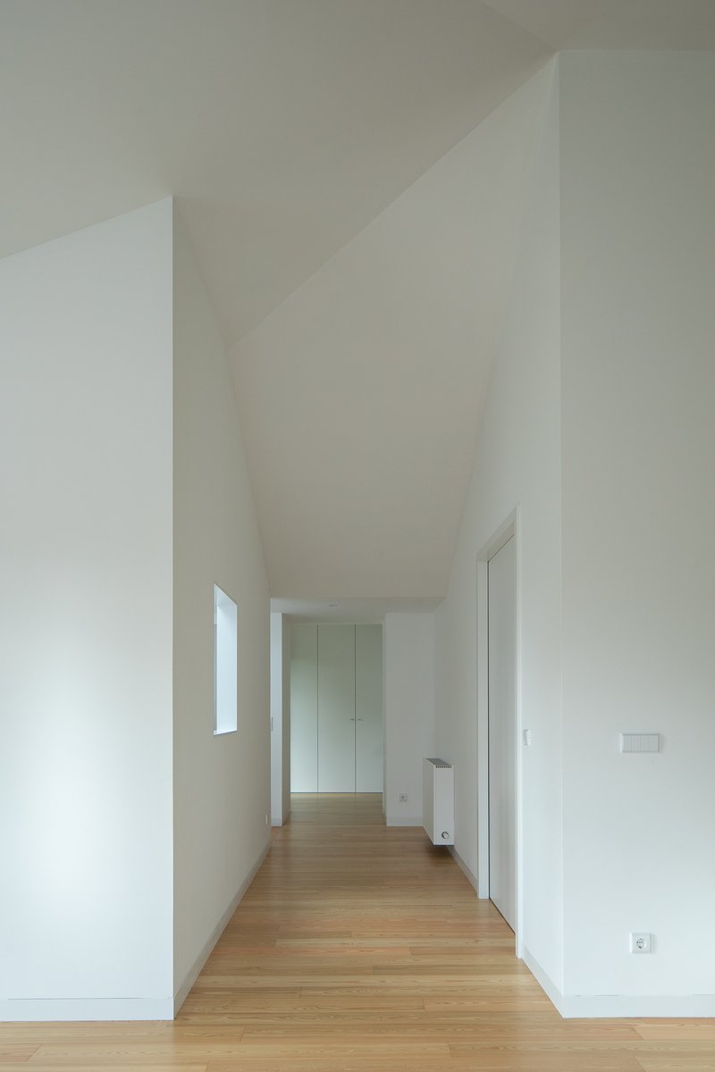 Corridor with angled ceiling planes, oak flooring, and tall vertical window casting natural light