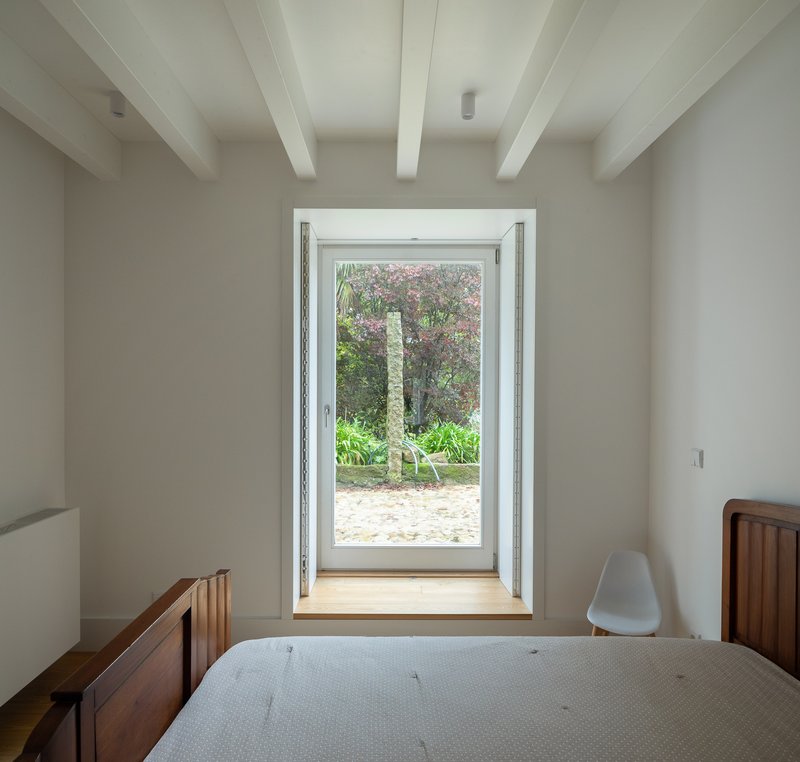 Bedroom with exposed white beams and framed door opening to garden courtyard with palm tree