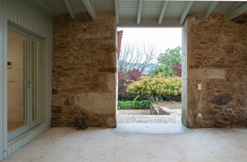 Covered entrance passage with exposed stone walls and painted timber ceiling beams framing a garden view
