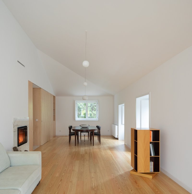 Open living space with oak flooring and vaulted ceiling connecting to a dining area with pendant lights