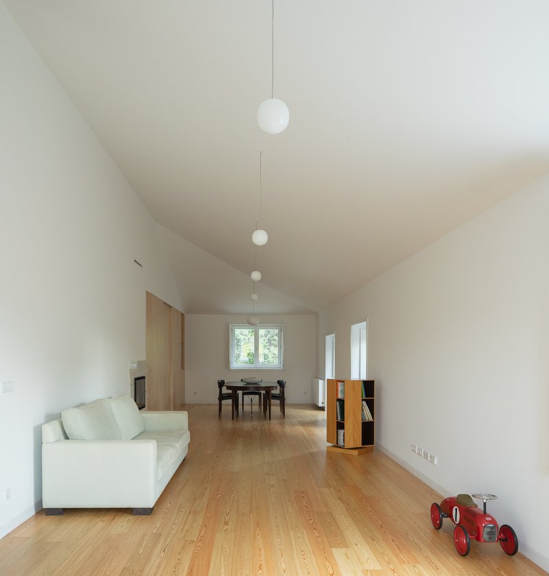 Open living space with oak flooring, vaulted ceiling and pendant lights suspended in a row