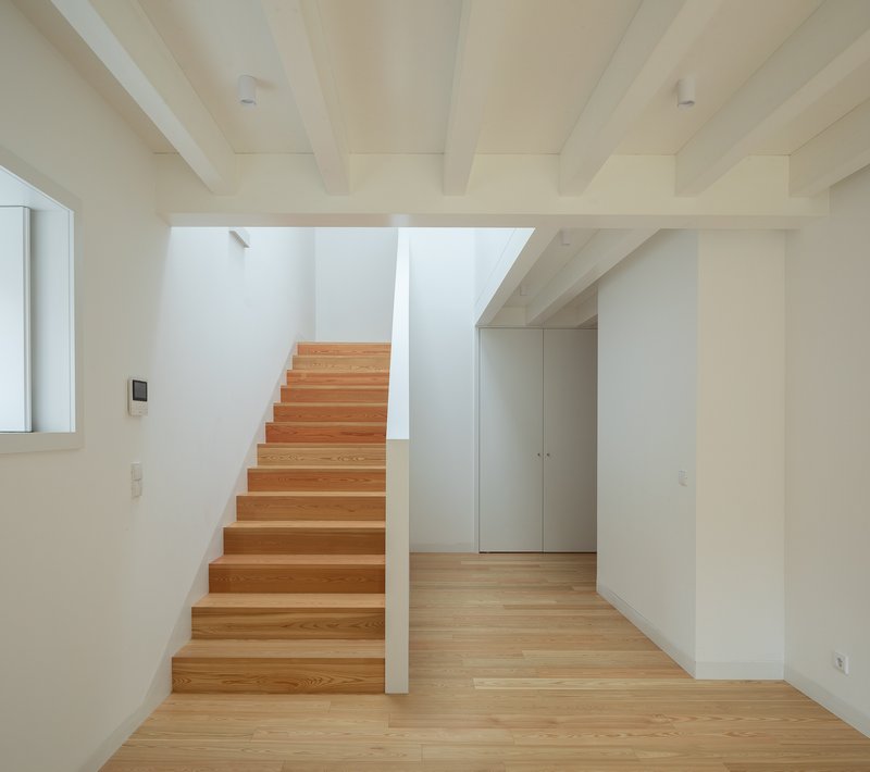 Timber staircase with exposed ceiling beams rising through a double-height volume with wood flooring