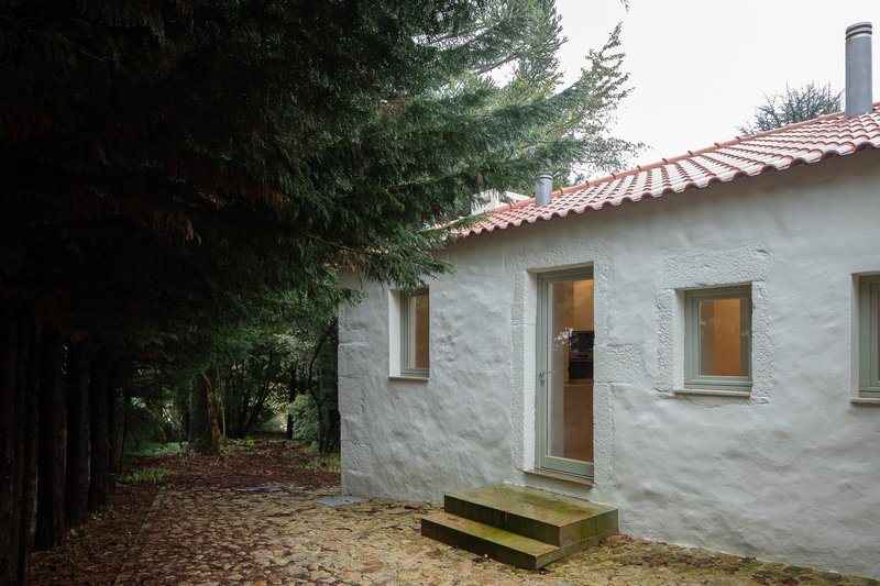 White rendered facade with timber-framed windows and terracotta tile roof beside evergreen trees