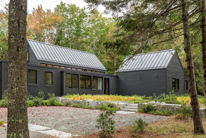 Two gabled volumes connected by a glazed link with terraced granite steps and planted beds between trees