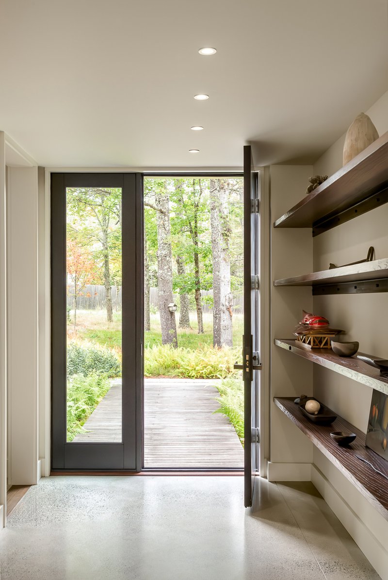 Entry hall with glazed door opening to a timber boardwalk through the forest and timber shelving along one wall