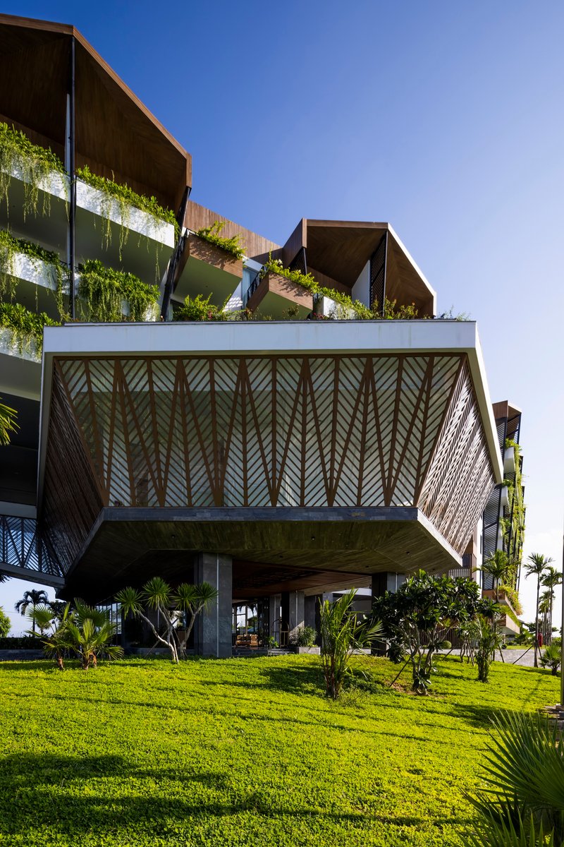 Cantilevered upper floor with herringbone timber screens suspended above a grass lawn and palm trees