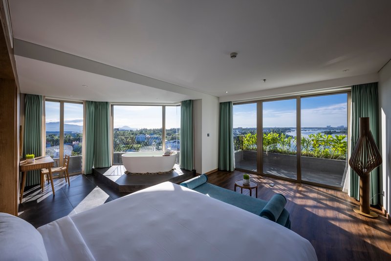 Hotel bedroom with floor-to-ceiling windows opening to a planted balcony with mountain views