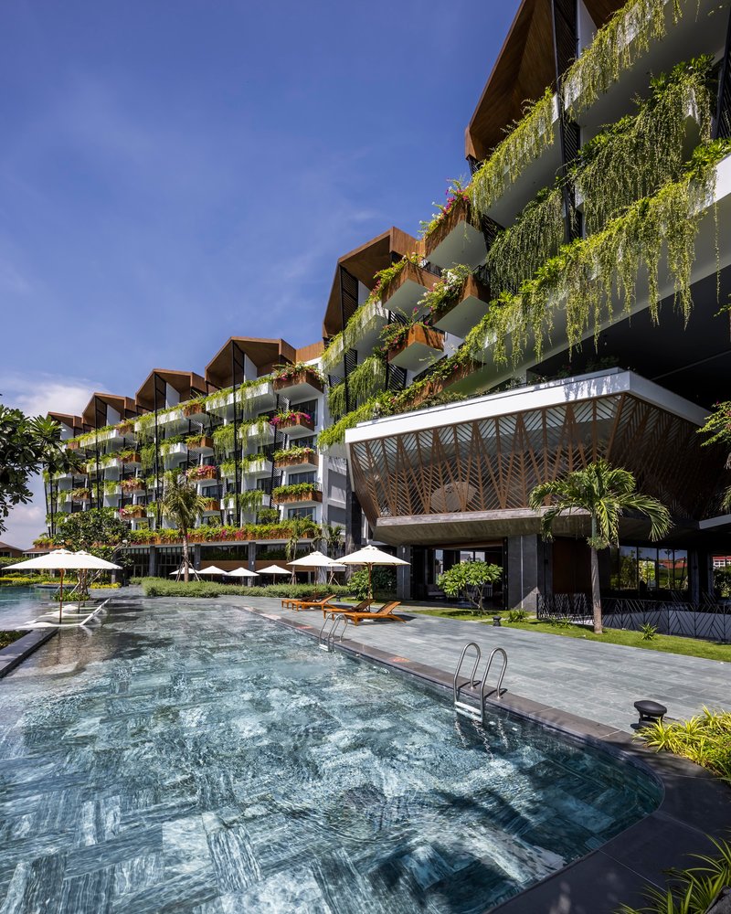 Multi-story facade with cascading planted balconies above a ground-level swimming pool under clear blue sky