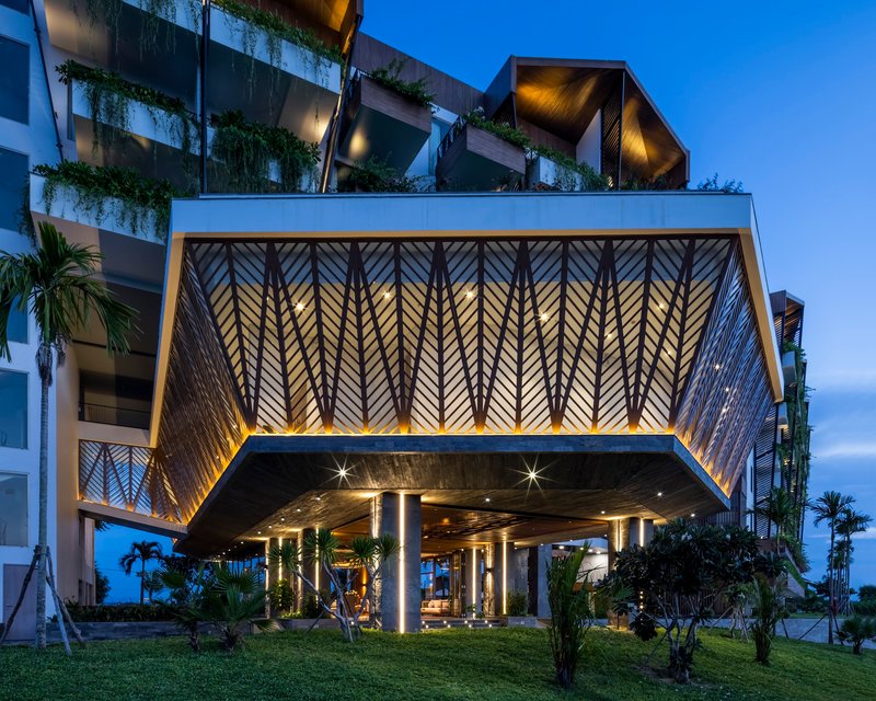Cantilevered porte-cochère with backlit chevron-patterned metal screens and planted terraces above at blue hour