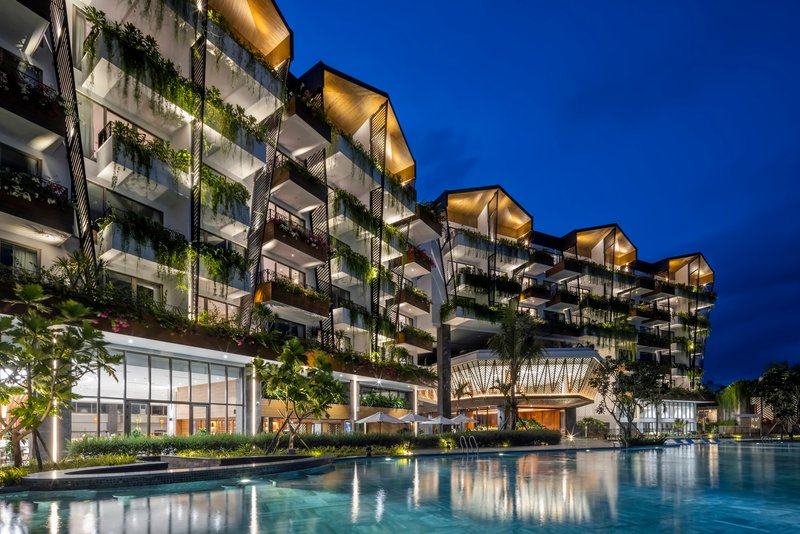 Residential tower facade with planted balconies and illuminated overhangs reflected in the pool at dusk