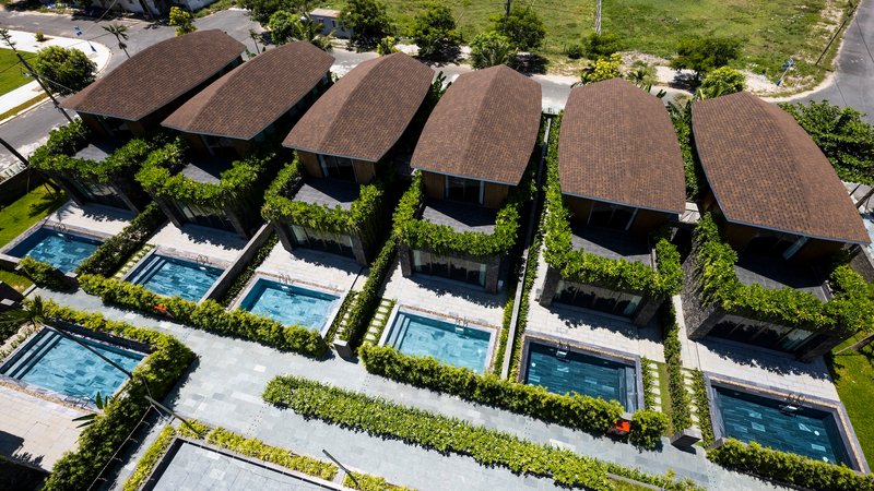 Aerial view of five villas with curved roofs arranged in a row beside individual pools