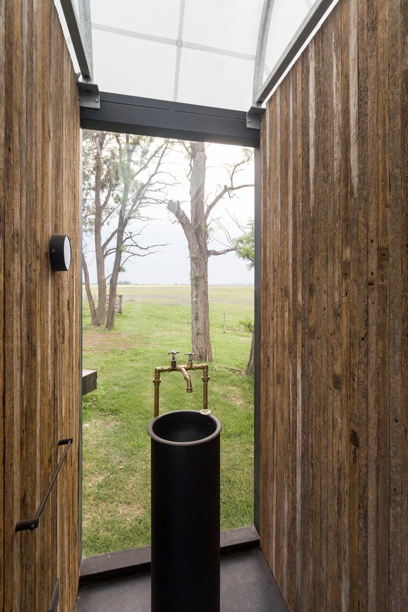 Narrow bathroom with vertical timber cladding, skylight, and cylindrical black basin facing open landscape