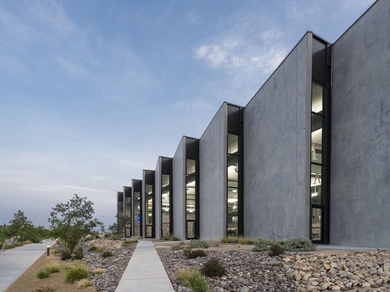 Illuminated vertical glazing slots between concrete fins at dusk with xeriscape planting