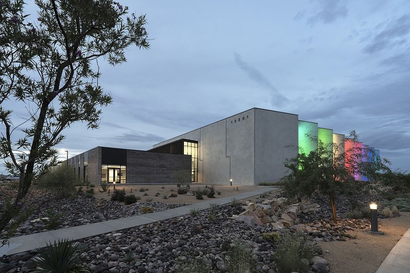 Concrete and brick volumes with illuminated vertical fins and desert landscaping at dusk