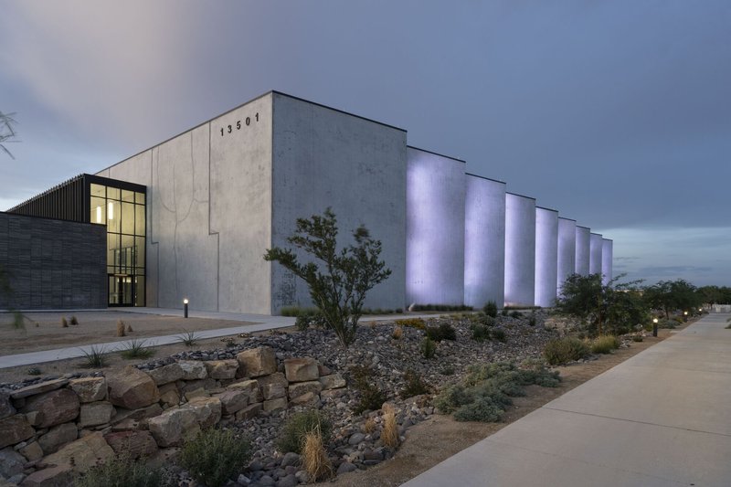 Concrete facade with uplighting on vertical fins beside a gravel landscape bed and sidewalk