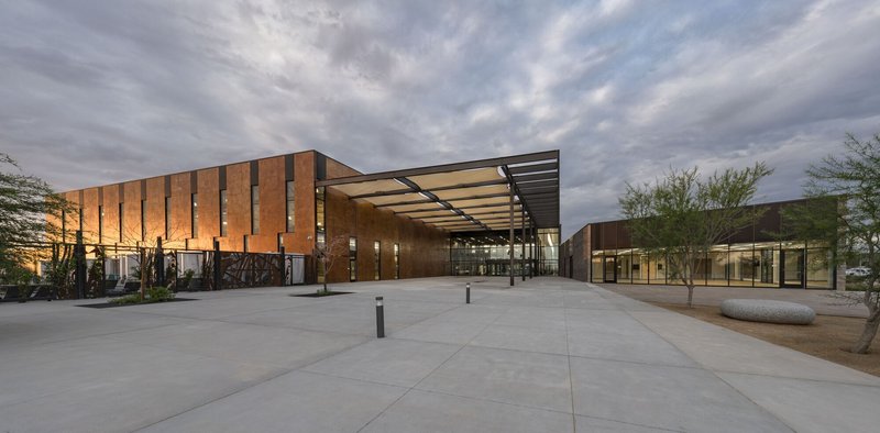 Glass entry pavilion with projecting canopy flanked by timber screen walls at dusk