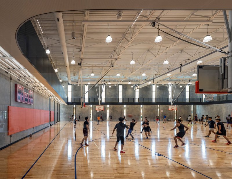 Indoor basketball court with wood floor, exposed steel trusses and players in motion