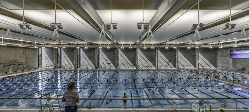 Long view of lap pool with repeated diagonal concrete buttresses and a single swimmer