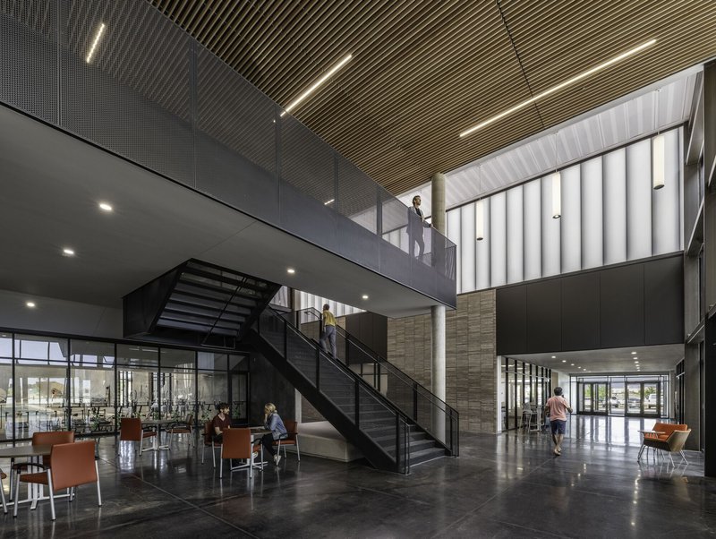 Double-height lobby with black steel staircase, slatted wood ceiling and visitors below