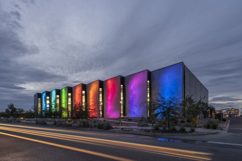 Concrete facade with vertical illuminated slots in spectrum colors at dusk with car light trails