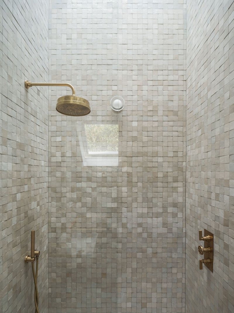 Shower enclosure lined with small white mosaic tiles and brass fixtures