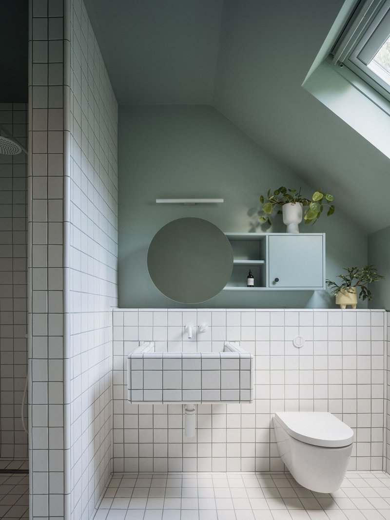 Bathroom interior showing white tiled walls, sloped ceiling with skylight, and sage green painted surfaces