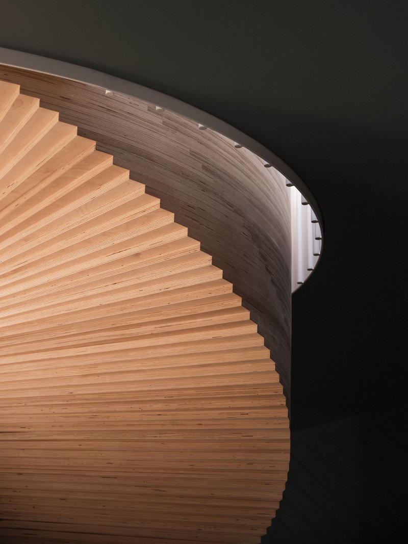 Looking up at the curved timber staircase with horizontal slats wrapping around a cylindrical void