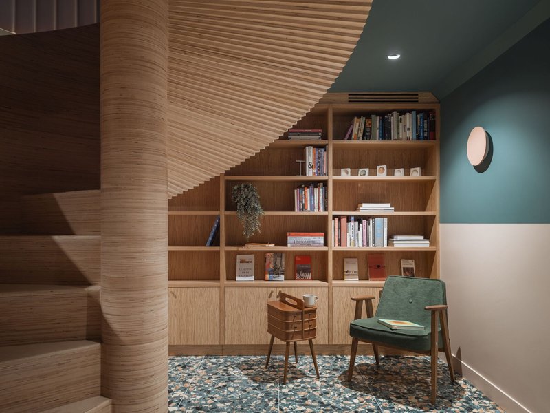 Reading nook beneath the spiral timber staircase with built-in oak shelving and terrazzo floor tiles