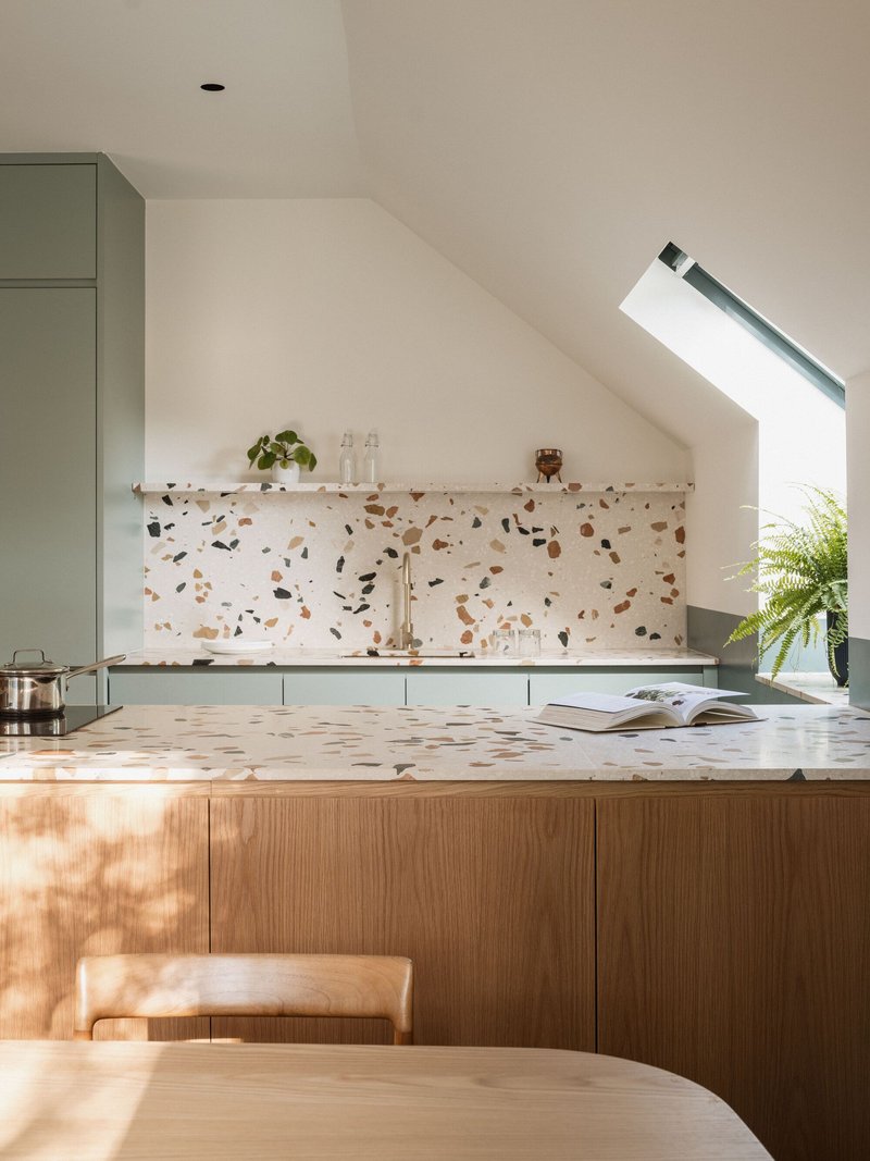 Kitchen island with terrazzo countertop and backsplash beneath an angled skylight in morning light
