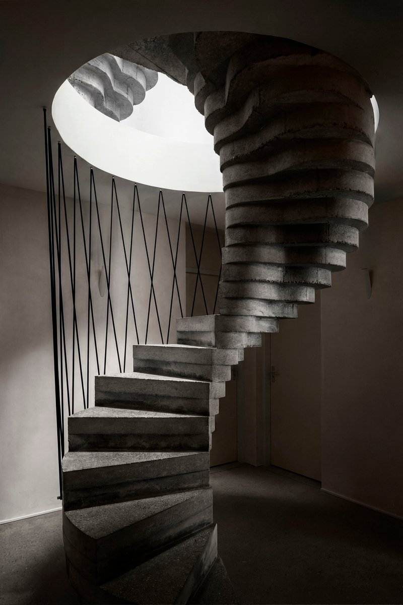 View up the spiral concrete staircase with zigzag steel balustrade beneath a circular skylight