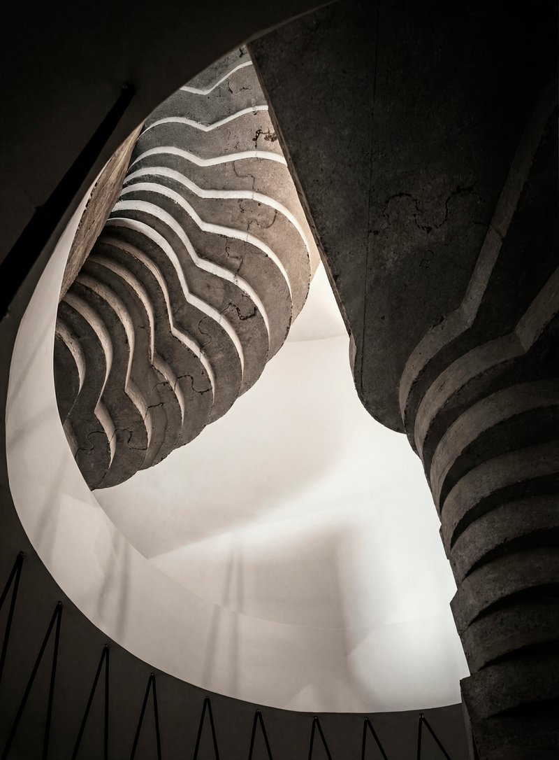 Looking up at the spiraling concrete staircase with wavy formwork patterns under natural light