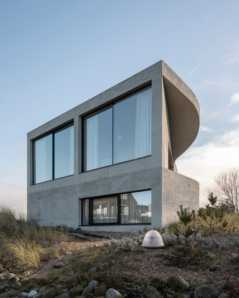 Rear facade at dusk with large glazed openings and cylindrical roof element above planted dunes