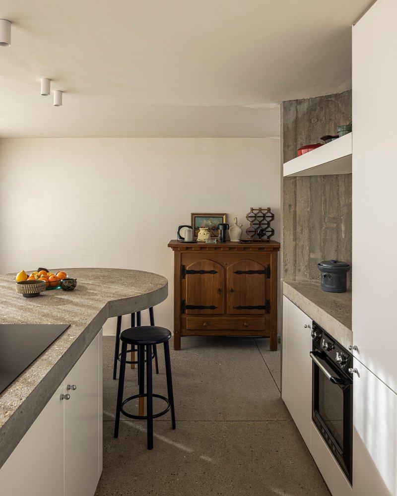 Kitchen with curved concrete island, terrazzo floor, and board-formed concrete wall in natural light