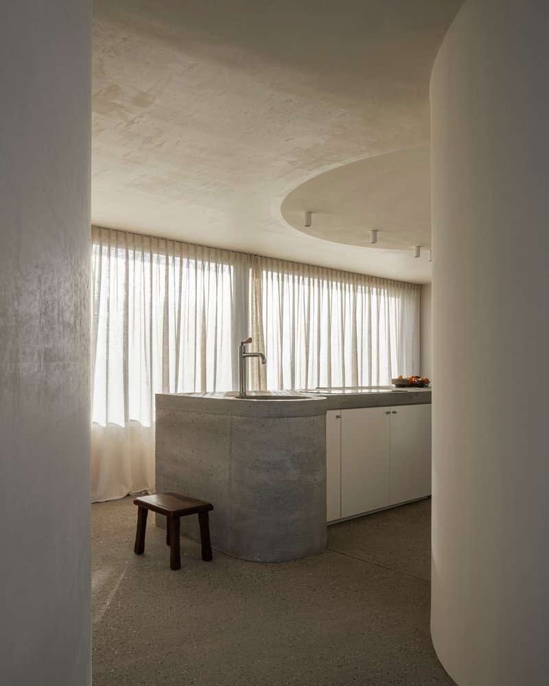 Arched doorway framing kitchen counter with board-formed concrete base and full-height curtained window