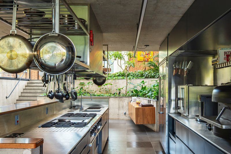 Galley kitchen with stainless steel appliances, exposed concrete ceiling and hanging cookware overlooking a planted terrace