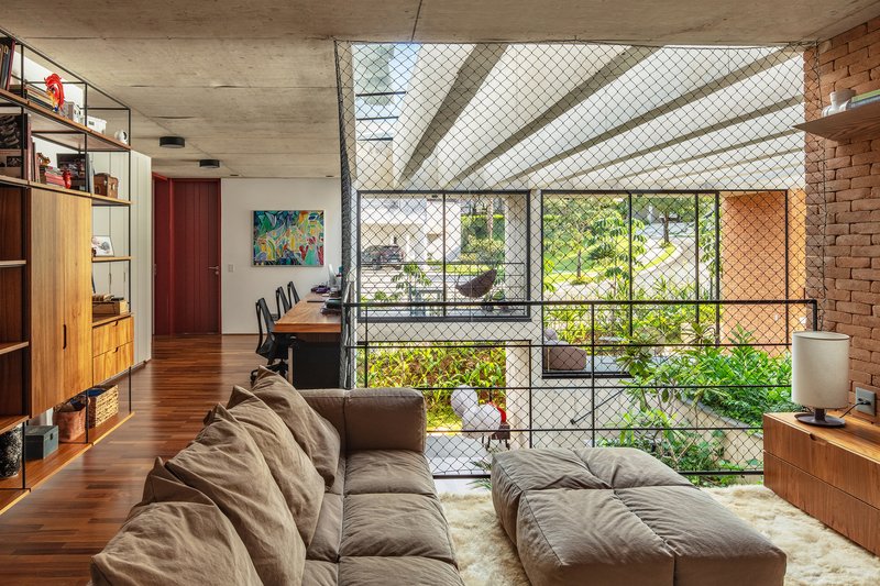 Living room with chain-link safety screen on mezzanine opening, exposed brick wall and timber built-in shelving