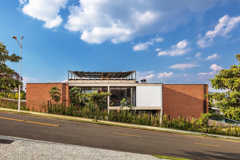 Facade composition with brick volumes, white panel, planted verge and exposed roof structure under blue sky