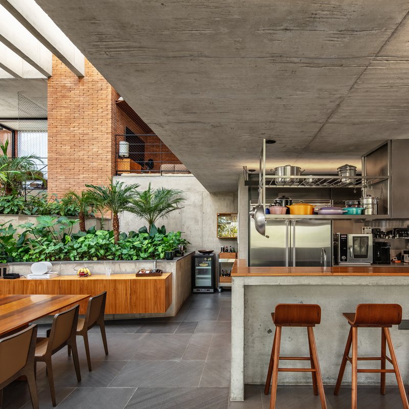 Open kitchen with stainless steel shelving and concrete island beneath angular ceiling beside planted wall