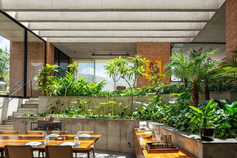 Dining area with timber table facing tiered concrete planters filled with foliage beneath skylight