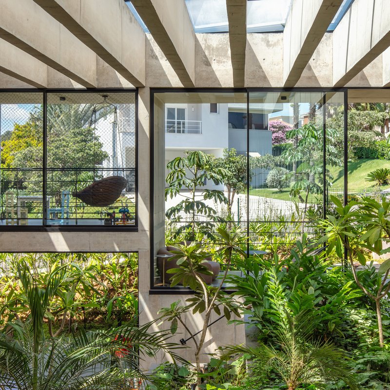 Covered planted courtyard with concrete beams overhead and floor-to-ceiling glazing framing garden views