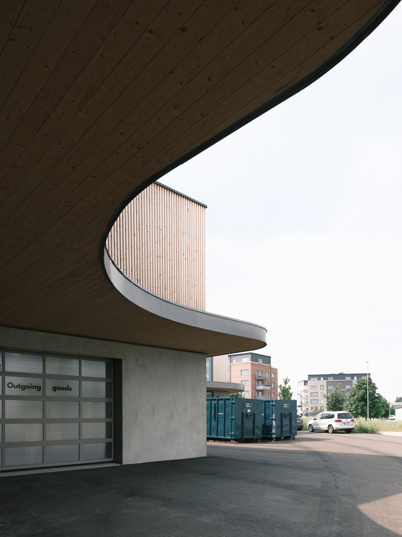 Curved timber-clad volume emerging from beneath a deep roof overhang with exposed wood soffit