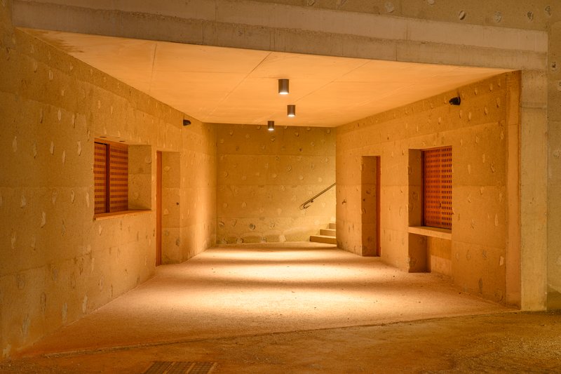 Interior corridor with rammed earth walls, wood shutters and warm light spilling across the floor at dusk