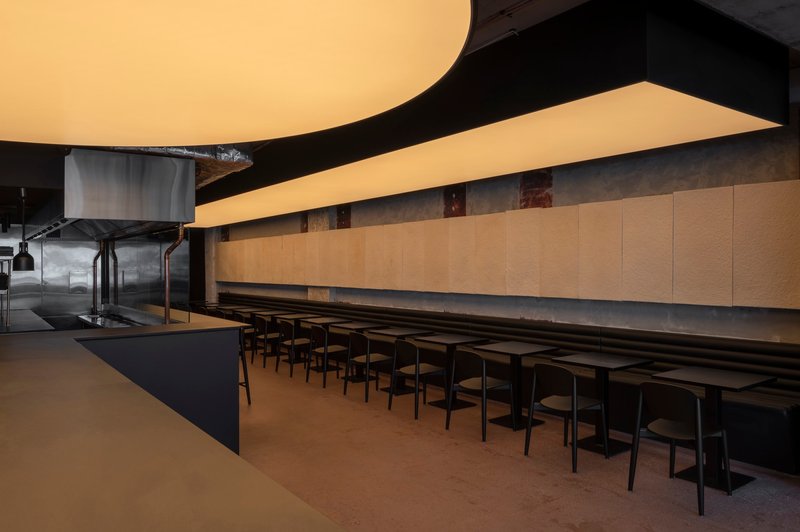Interior dining space with curved luminous ceiling panels above a long communal table and black chairs