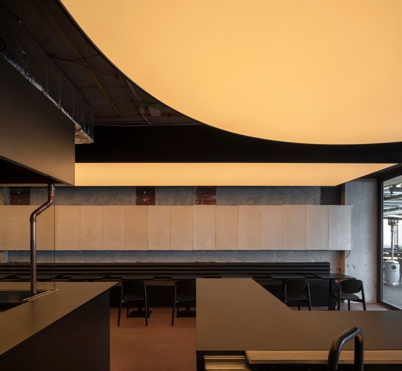 Dining area with wood panel wall and exposed black piping below a curved ceiling element
