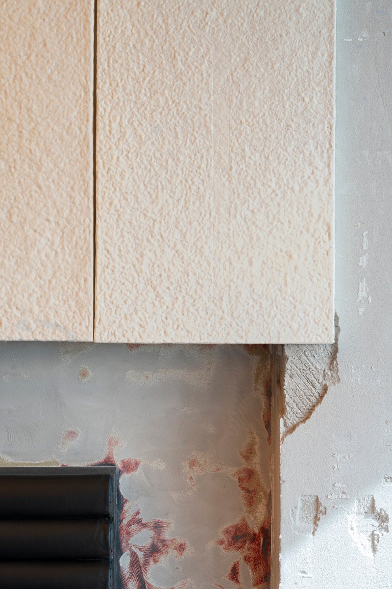 Detail of textured cream panels meeting a distressed white wall with exposed rust marks