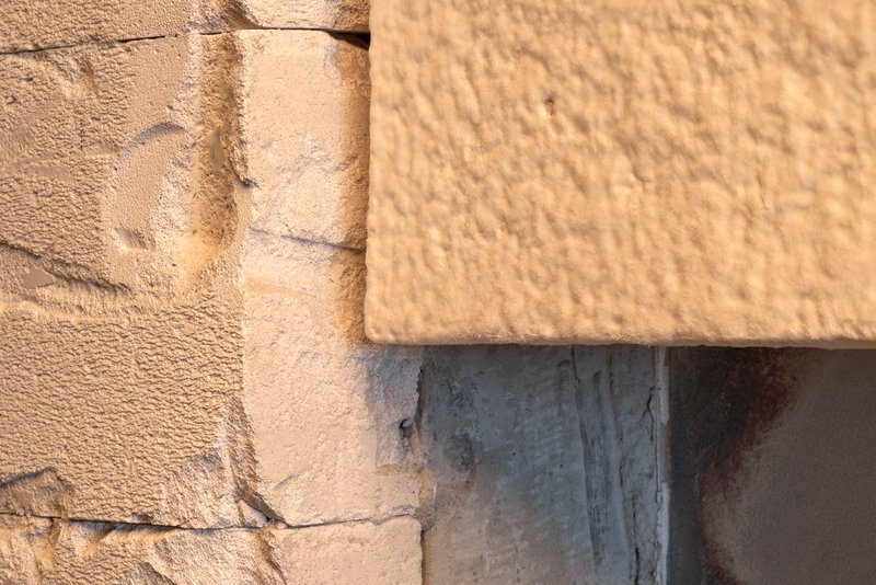Close-up of stone and concrete junction with textured cream panel in warm sunlight