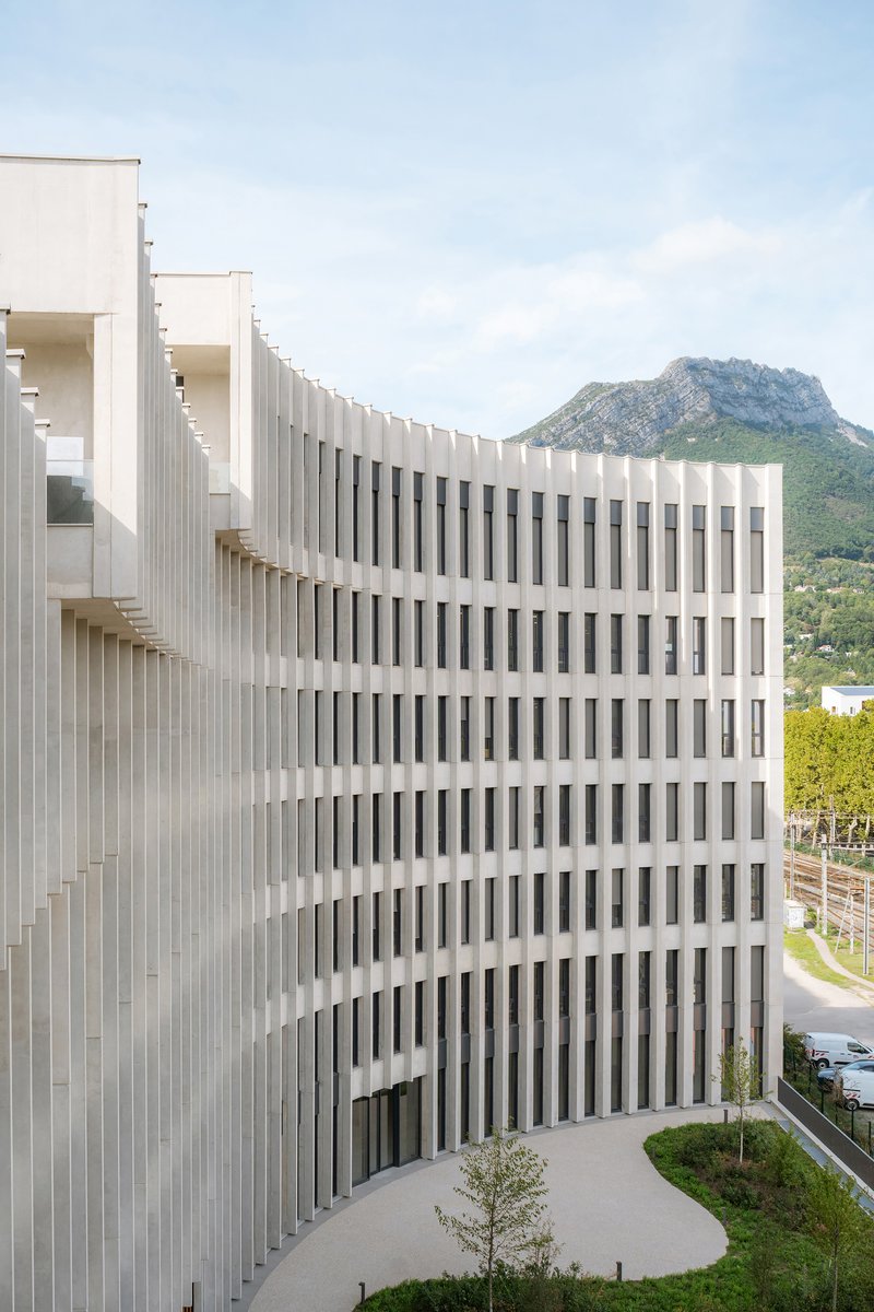 White vertical fin facade curving along the building volume with a mountain backdrop