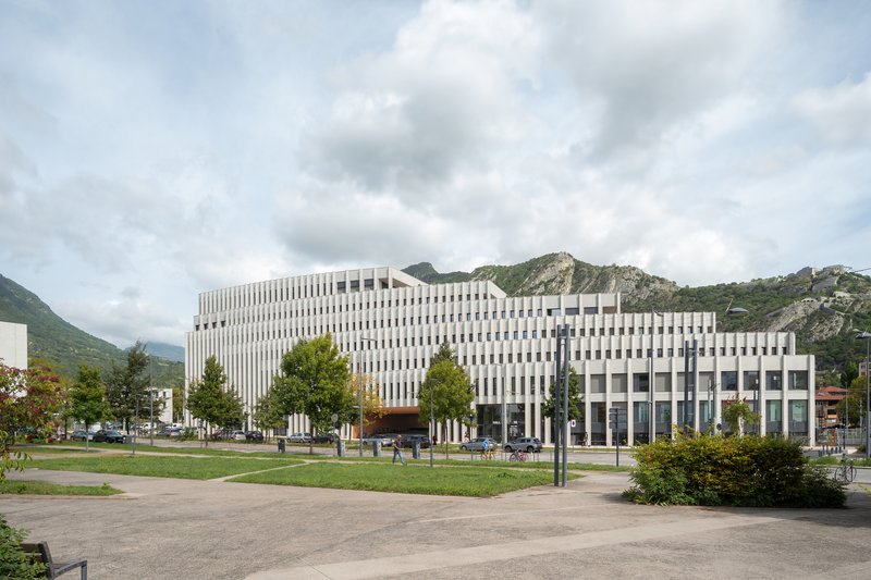 View across the park lawn showing the terraced facade stepping down against the mountains