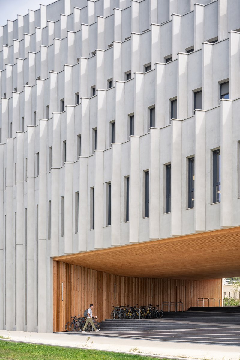 Covered entrance with timber soffit and vertical white fins above a cyclist passing on the path