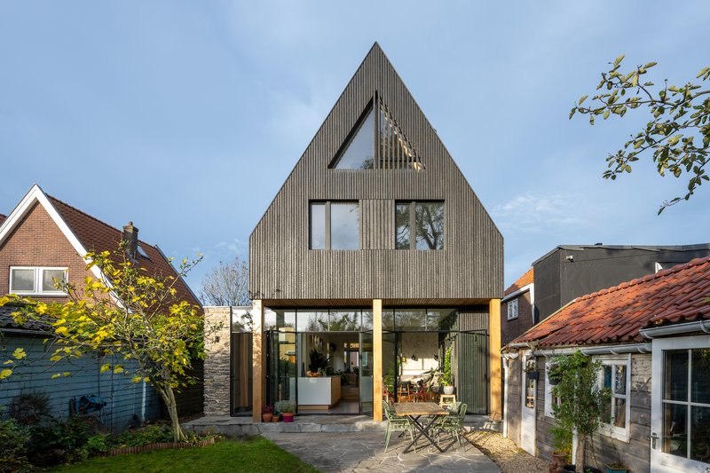 Rear garden view of the steeply pitched gable with vertical cladding and timber-framed canopy